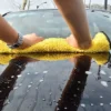 Eine Person reinigt ein Auto mit einem gelben Mikrofaser-Reinigungshandtuch.